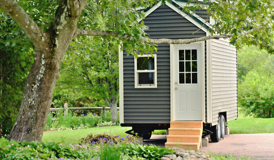 Tiny House auf Rädern neben einem Baum.