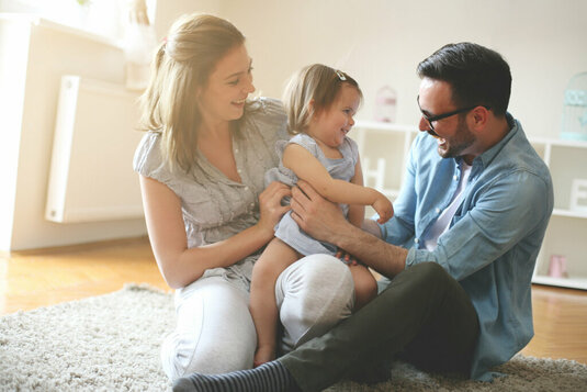 Glückliche Familie sitzt auf dem Fussboden mit ihrer Tochter.