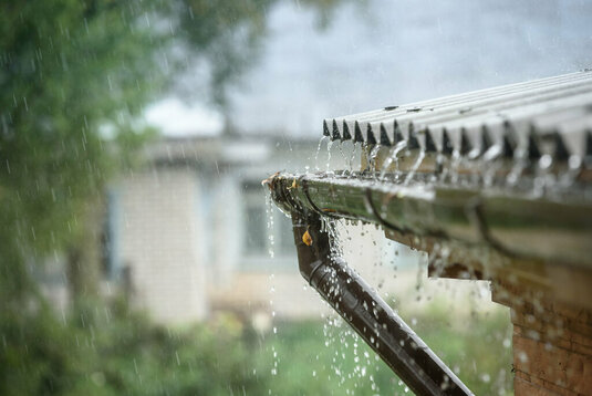 Regenwasser läuft von einem Flachdach mit Dachrinne ab.