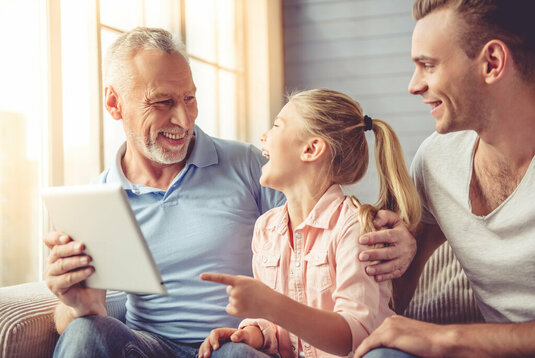 Opa, Vater und Tochter sitzen glücklich mit Tablet auf der Couch.