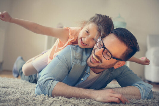 Vater und Tochter spielen im Wohnzimmer.