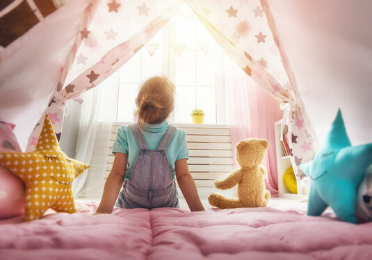 Kind mit Teddybär auf einem Bett