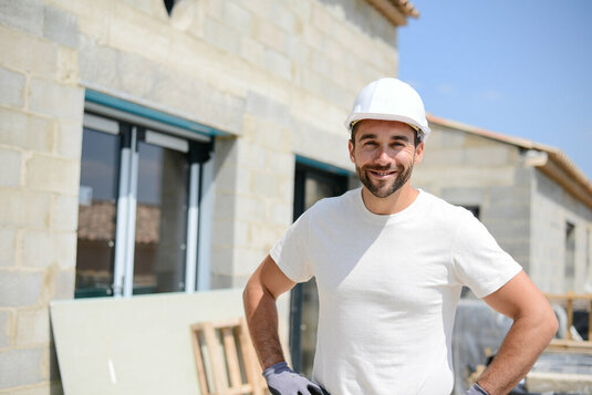 Freundlicher Handwerker vor einem Rohbau.