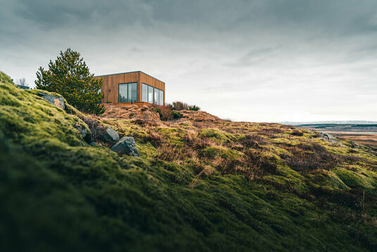 Ein winziges Haus auf einem grasbewachsenen Hügel, perfekt für einen einsamen Urlaub oder einfach nur für eine friedliche Entspannung in Verbindung mit der Natur. Moderne Architektur in den skandinavischen Ländern.