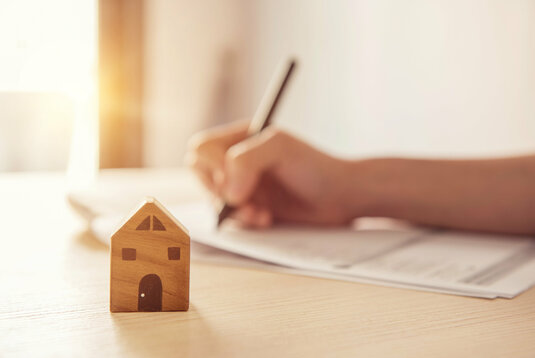 Holzspielzeug Haus mit Frau unterzeichnet einen Kaufvertrag oder Hypothek für ein Haus, Immobilien-Konzept.