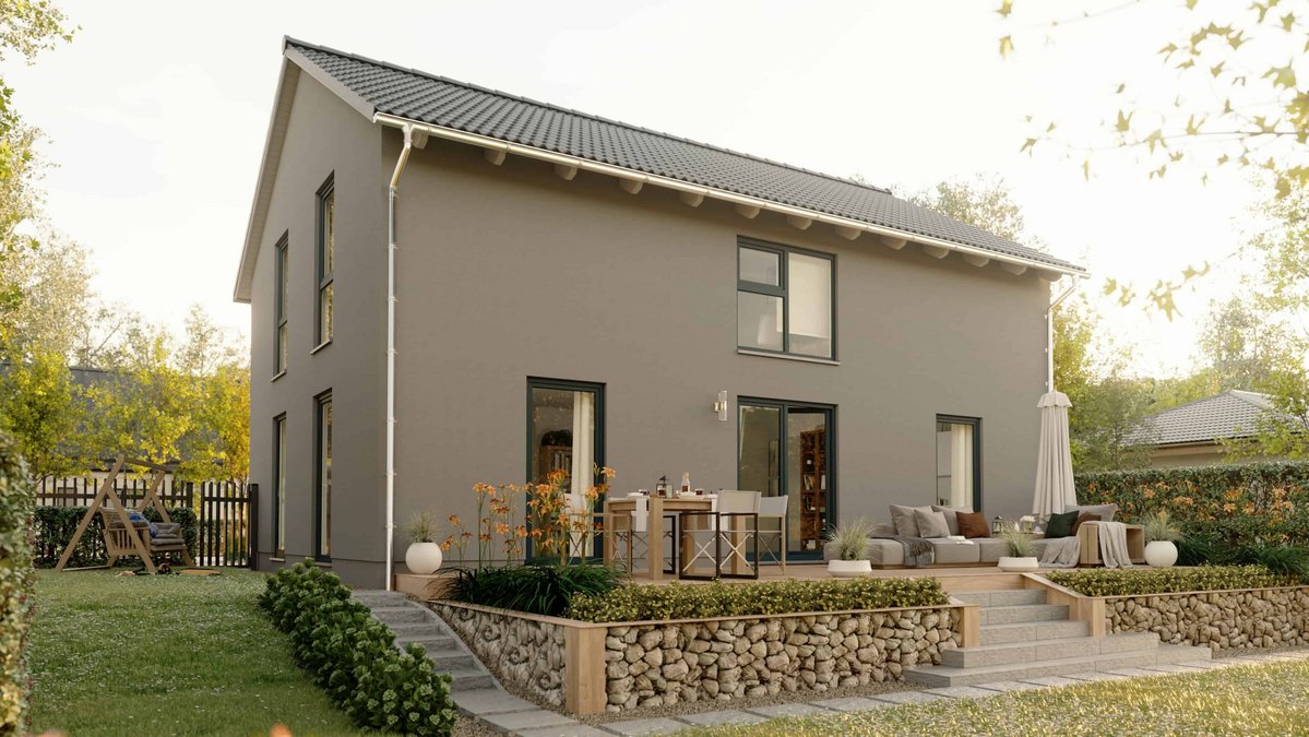 Town & Country Massivhaus mit heller Fassade Terrasse und gemütlich eingerichtetem Garten. Abgebildet ist das Einfamilienhaus Landhaus 142 Modern Elegance. Steht für sicheres Bauen mit Festpreis Bauzeitgarantie und Hausbau Schutzbrief.