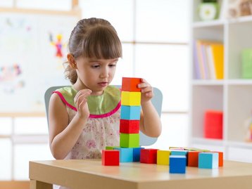 Bauphase Qualität und Insolvenzschutz gesichert Mädchen stapelt erste Bausteine konzentriert, symbolisiert gesicherte Bauphase mit Qualität, 20 Prozent Fertigstellungsbürgschaft und Treuhand Baugeldkonto